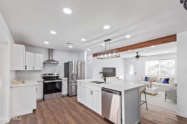 kitchen with white cabinets, wall chimney range hood, sink, an island with sink, and appliances with stainless steel finishes