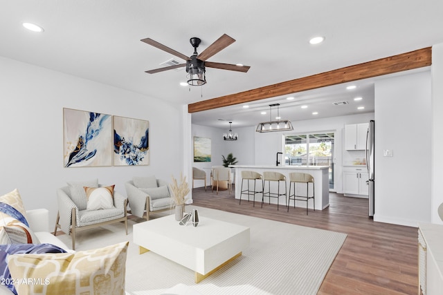 living room featuring beamed ceiling, wood-type flooring, and ceiling fan with notable chandelier