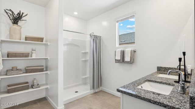 full bathroom featuring double vanity, baseboards, a stall shower, and a sink