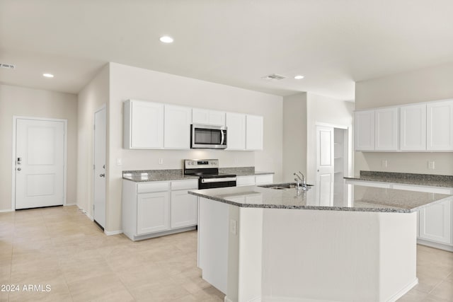 kitchen with light stone countertops, a center island with sink, appliances with stainless steel finishes, white cabinetry, and a sink