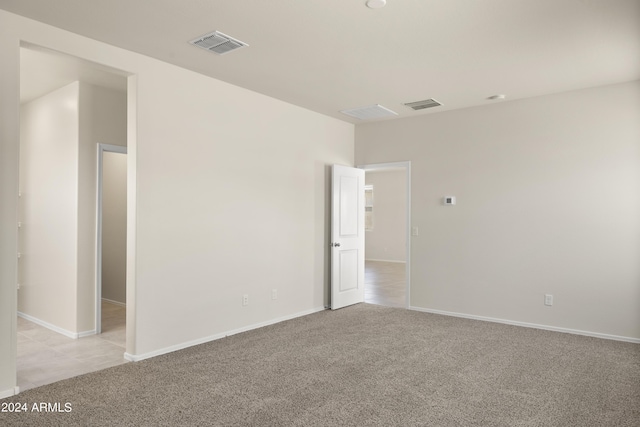 empty room with baseboards, visible vents, and light carpet