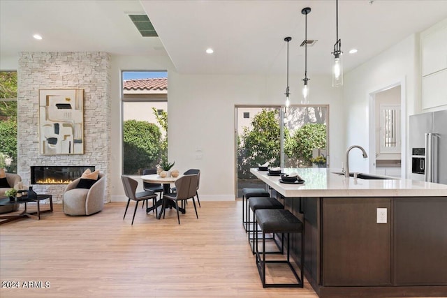 kitchen with visible vents, light wood-style flooring, light countertops, a stone fireplace, and a sink