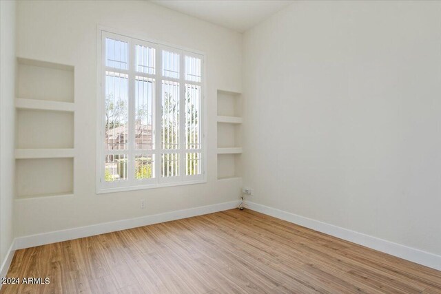 spare room featuring built in shelves and light hardwood / wood-style floors