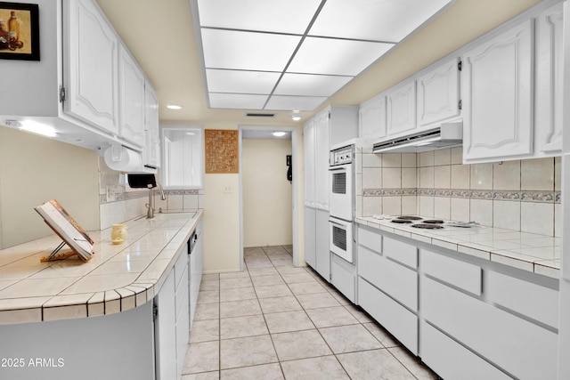 kitchen featuring under cabinet range hood, tile counters, white cabinets, and a sink