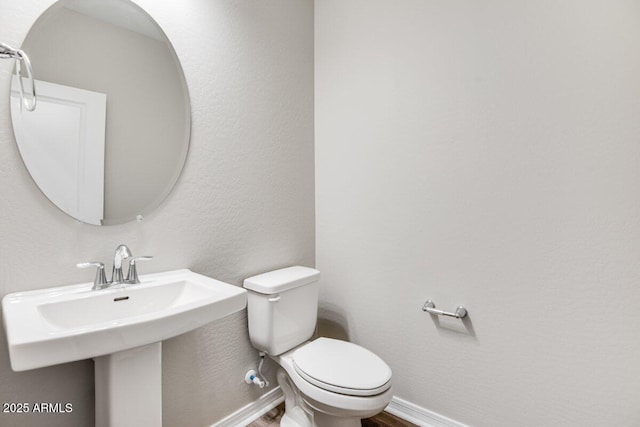 half bath featuring a sink, wood finished floors, toilet, and baseboards