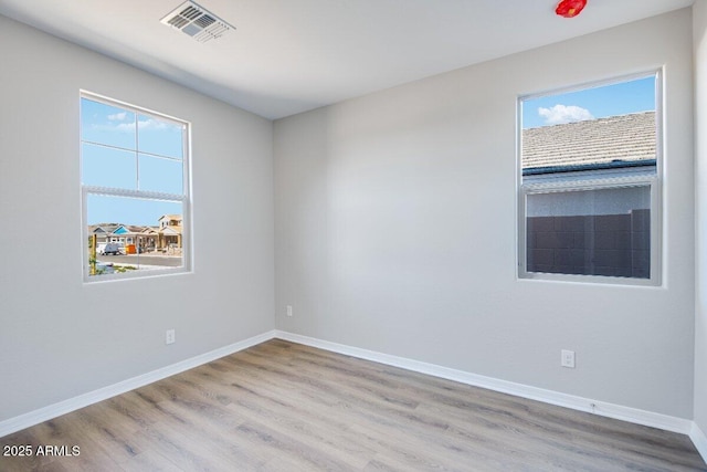 empty room with baseboards, wood finished floors, visible vents, and a healthy amount of sunlight