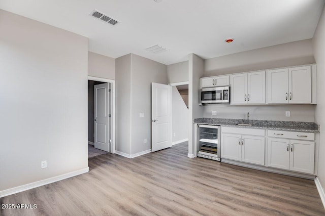 kitchen with light wood finished floors, beverage cooler, visible vents, stainless steel microwave, and a sink