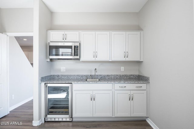 kitchen featuring light stone counters, beverage cooler, baseboards, white cabinets, and stainless steel microwave