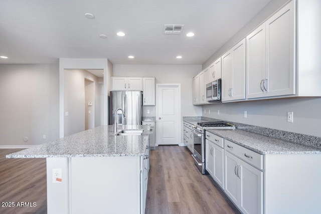 kitchen featuring visible vents, an island with sink, appliances with stainless steel finishes, wood finished floors, and a sink