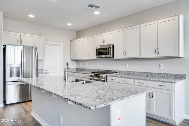 kitchen featuring visible vents, an island with sink, appliances with stainless steel finishes, wood finished floors, and a sink