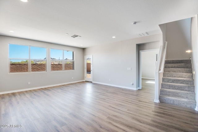 unfurnished living room with stairs, wood finished floors, visible vents, and baseboards