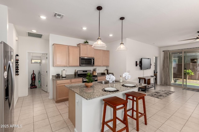 14233 W Georgia Dr, Surprise, AZ 85379 - kitchen featuring appliances with stainless steel finishes, light brown cabinetry, light tile patterned flooring, a kitchen bar, and ceiling fan