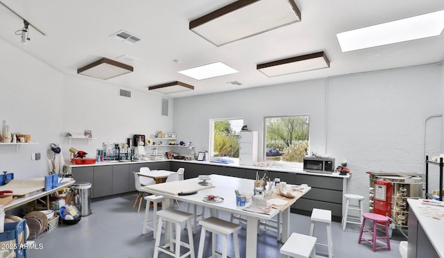 kitchen with concrete flooring, stainless steel microwave, visible vents, and gray cabinetry