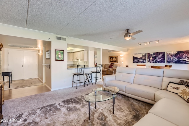 living area featuring visible vents, carpet flooring, ceiling fan, a textured ceiling, and baseboards