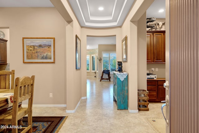 corridor featuring light tile patterned floors and a tray ceiling