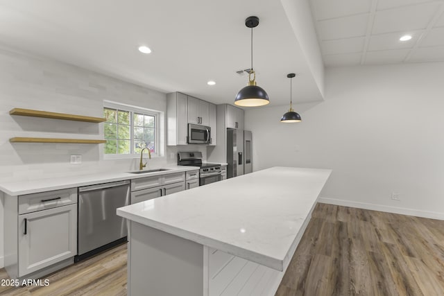 kitchen with appliances with stainless steel finishes, wood finished floors, gray cabinetry, a sink, and recessed lighting