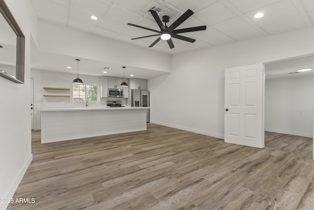 unfurnished living room featuring a ceiling fan, a sink, light wood finished floors, and baseboards