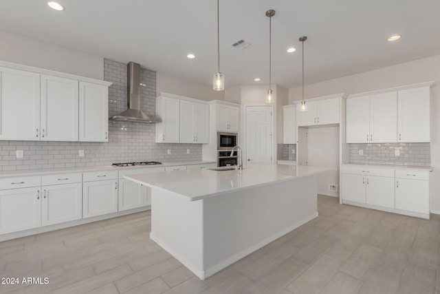 kitchen with white cabinetry, wall chimney range hood, stainless steel appliances, and an island with sink