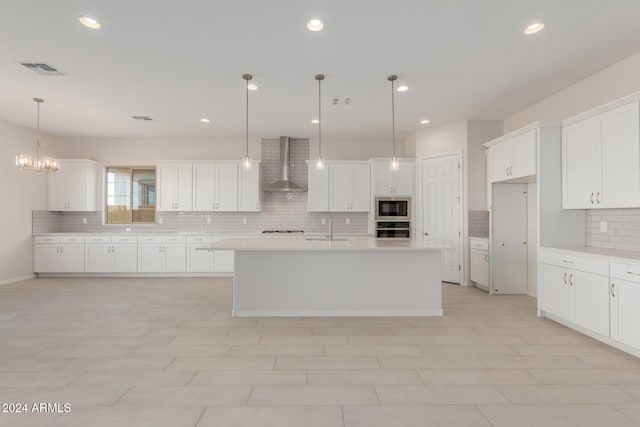 kitchen with appliances with stainless steel finishes, sink, wall chimney range hood, decorative light fixtures, and a center island with sink