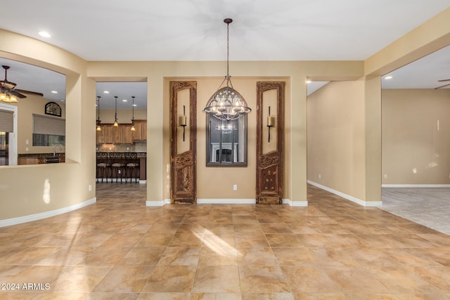 unfurnished dining area with sink and ceiling fan with notable chandelier