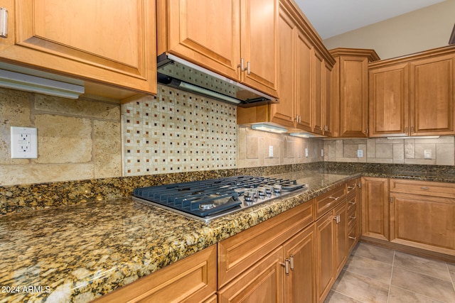 kitchen with light tile patterned flooring, stainless steel gas stovetop, decorative backsplash, and dark stone counters