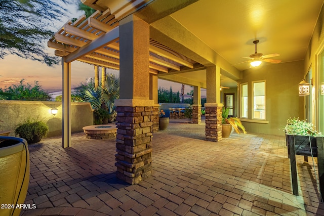 patio terrace at dusk with ceiling fan, an outdoor fire pit, and a pergola