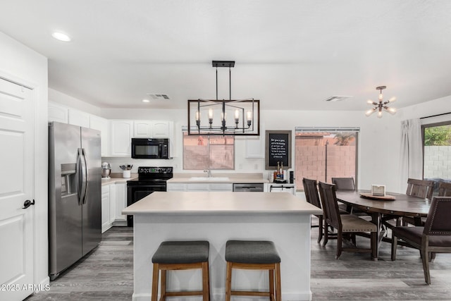 kitchen featuring white cabinetry, a kitchen island, a notable chandelier, and black appliances