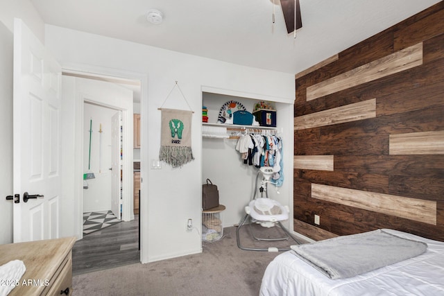 carpeted bedroom with ceiling fan, wooden walls, and a closet