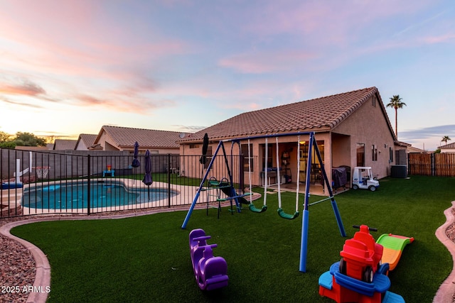 playground at dusk featuring central AC unit, a yard, a patio area, and a fenced in pool