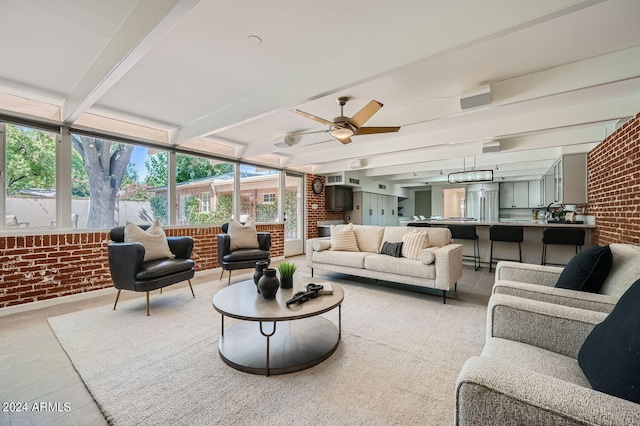 living room with beam ceiling, ceiling fan, and brick wall