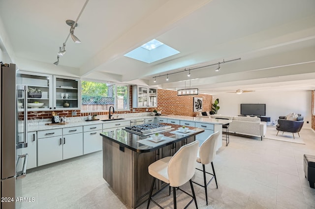 kitchen featuring white cabinets, a skylight, sink, a kitchen island, and decorative backsplash