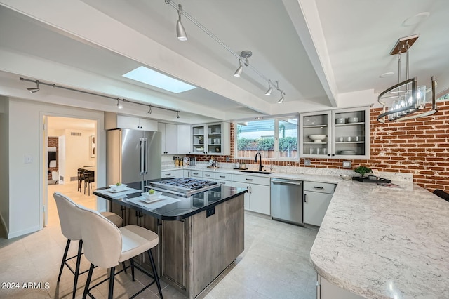 kitchen featuring brick wall, appliances with stainless steel finishes, sink, and white cabinetry