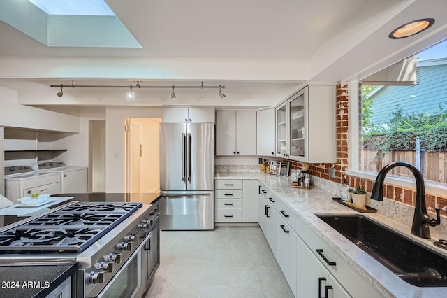 kitchen featuring light stone counters, sink, white cabinets, appliances with stainless steel finishes, and washing machine and dryer