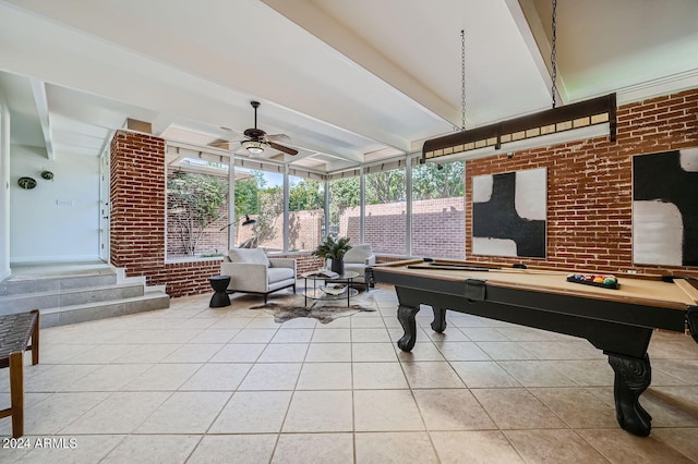 recreation room featuring ceiling fan, beamed ceiling, brick wall, and light tile patterned flooring