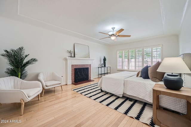 bedroom featuring ceiling fan, a brick fireplace, and light hardwood / wood-style floors