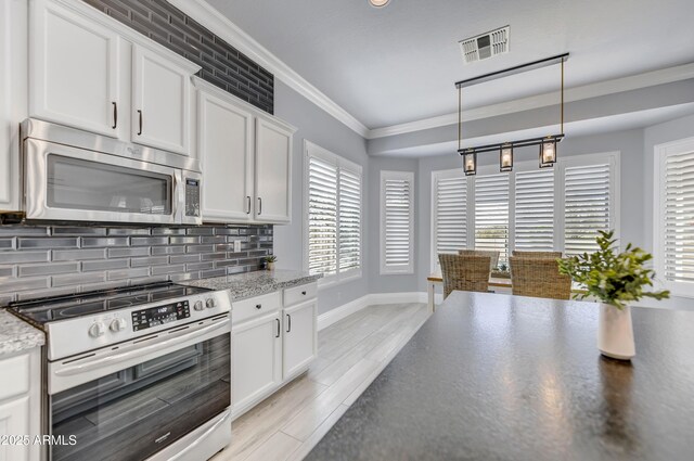 kitchen featuring appliances with stainless steel finishes, decorative backsplash, baseboards, white cabinets, and ornamental molding