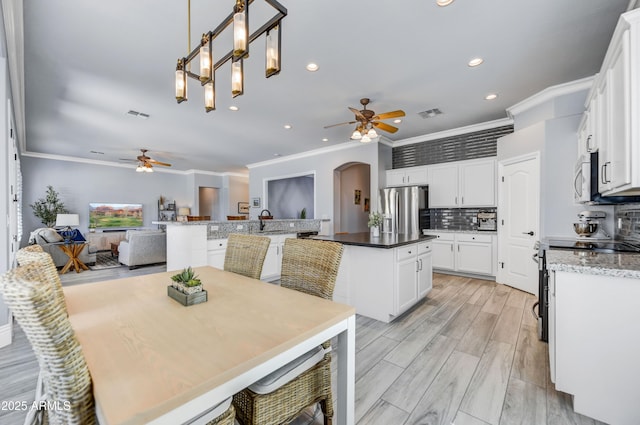 kitchen with ceiling fan, ornamental molding, stainless steel appliances, a kitchen island, and arched walkways