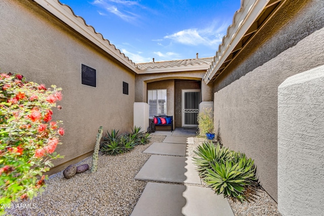 property entrance featuring stucco siding, a tile roof, and a patio