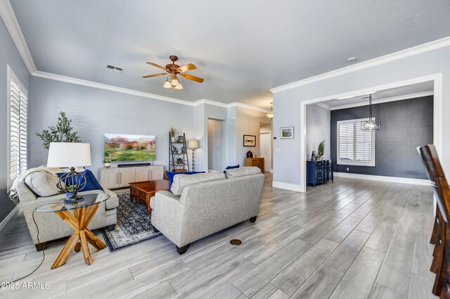 living area with light wood-style flooring, baseboards, a ceiling fan, ornamental molding, and a chandelier