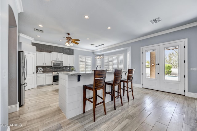 kitchen with stainless steel appliances, healthy amount of natural light, a ceiling fan, light wood-type flooring, and ornamental molding