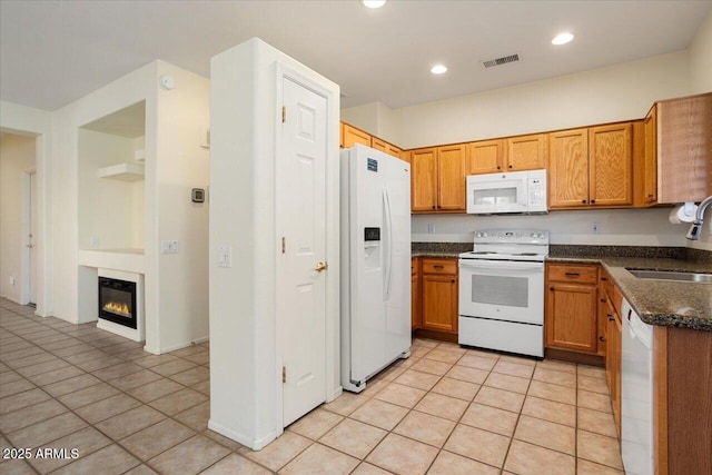 kitchen with dark stone countertops, sink, white appliances, and light tile patterned floors