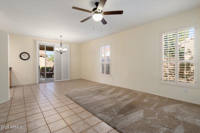 tiled empty room with plenty of natural light and ceiling fan with notable chandelier