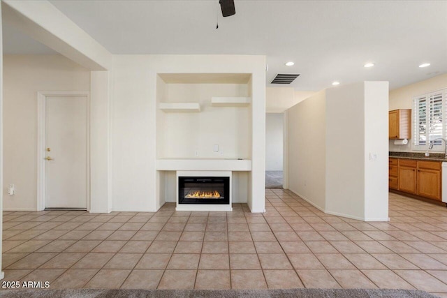 unfurnished living room featuring ceiling fan, sink, and light tile patterned floors