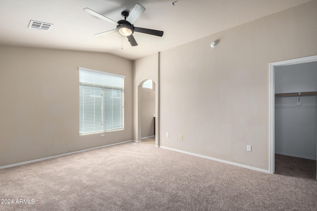 unfurnished bedroom featuring ceiling fan, a walk in closet, a closet, light colored carpet, and vaulted ceiling