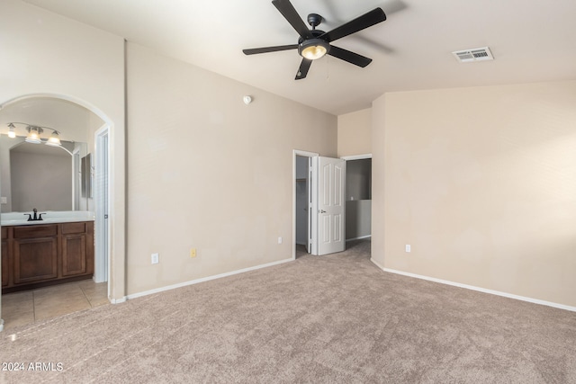 unfurnished bedroom featuring light carpet, ceiling fan, ensuite bathroom, and sink