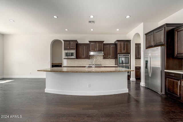 kitchen featuring dark brown cabinetry, an island with sink, stainless steel appliances, dark hardwood / wood-style floors, and decorative backsplash