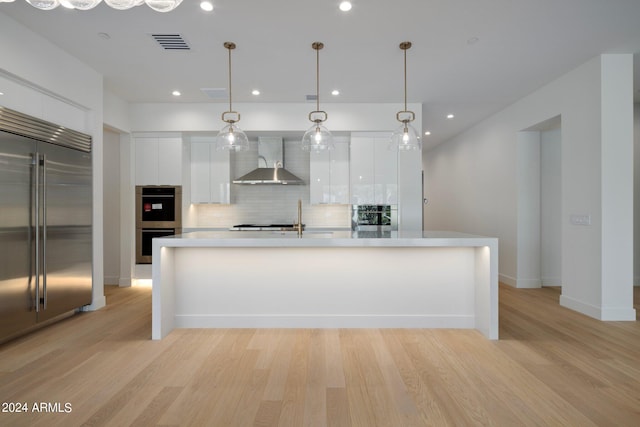 kitchen featuring light wood-type flooring, backsplash, wall chimney exhaust hood, white cabinetry, and appliances with stainless steel finishes