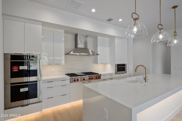 kitchen featuring wall chimney range hood, stainless steel appliances, light hardwood / wood-style floors, and white cabinets