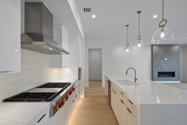 kitchen featuring decorative light fixtures, wall chimney range hood, a large fireplace, backsplash, and light wood-type flooring