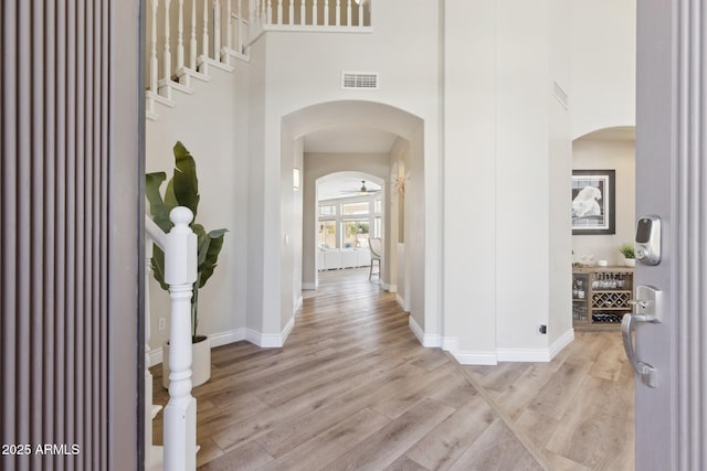 hallway featuring light wood-style floors, a high ceiling, visible vents, and arched walkways